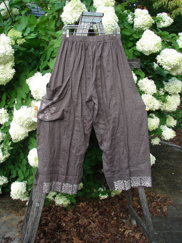 Susan Crawford Barclay Linen Single Crop Side Pocket Banded Bottom Pant in mocha, size 2, with a celtic floral print, hanging outdoors on a rack against white hydrangeas.