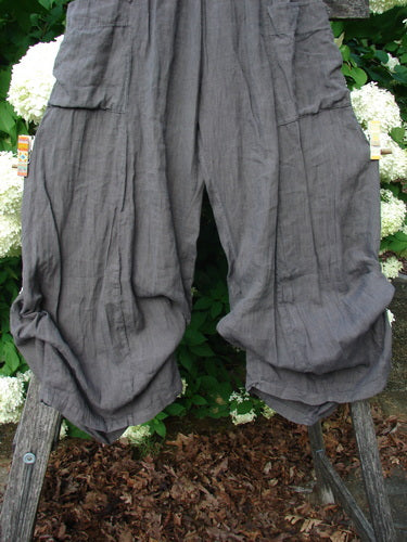 Bluefishfinder.com Barclay Linen Tie Bottom 4 Square Pant Cross Dye Army Unpainted Size 0 in textured gray linen, with wide gathered legs, tie hems, and square cargo-style pockets. The pants hang against leafy greenery, their soft crinkled fabric and muted cross-dyed finish emphasized by natural light.
