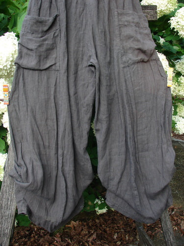 Bluefishfinder.com Barclay Linen Tie Bottom 4 Square Pant Cross Dye Army Unpainted Size 0, loose gray linen pants with a crinkled cross-dyed texture, square cargo pockets, and tie hems. They hang front-facing against dense green foliage and pale flowers.