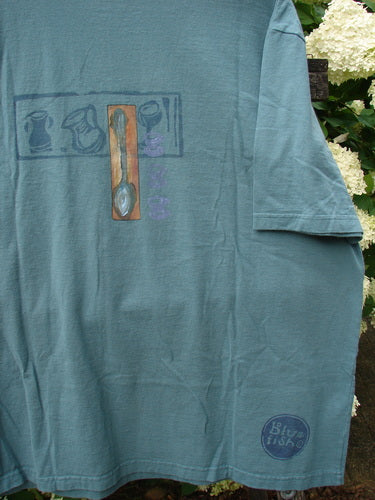 Bluefishfinder.com 2000 Artist Choice Short Sleeved Tee Steaming Teacup Green Mineral Size 2, a faded teal-green short-sleeve T-shirt with a small teacup graphic on the chest and a circular Bluefish logo near the hem. The soft, worn cotton hangs loosely, with a simple crew neck and matte, washed finish.