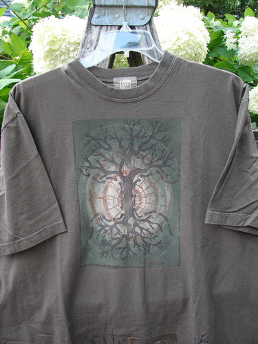 Bluefishfinder.com 2000 Short Sleeved Tee Earthen Tree Domino Size 2 in faded charcoal gray, with a soft crew neck and relaxed short sleeves. A centered earthy tree-and-domino graphic adds a muted, textured focal point against the washed cotton jersey.