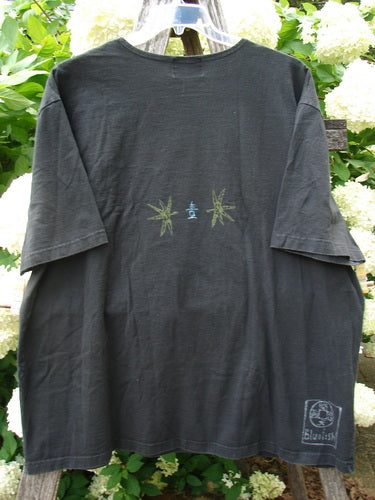 Bluefishfinder.com 1999 Short Sleeved Tee Geisha Gal in black, size 2, with a loose crewneck silhouette and faded short sleeves. The cotton tee hangs front-facing against leafy greenery, showing a small geisha graphic at the chest and a stamped logo near the hem.