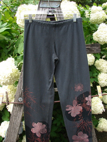 Bluefishfinder.com Barclay cotton-lycra leggings in off black, size 0, with a smooth elastic waistband and a slim, tapered silhouette. Pink daisy and twig floral prints cluster along the lower legs, hanging against a rustic wooden ladder amid bright white blossoms.