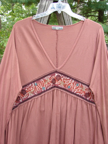 Barclay Decora Banded V Neck Dress Rouge Size 1 displayed on a hanger, highlighting its deep V-shaped neckline, sectional panels, and gentle vertical pleats, made from organic cotton with a unique upward bent banded accent.