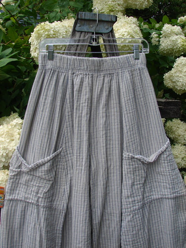 Bluefishfinder.com Barclay Gauze Crop Mojo Pant in unpainted sandy stripe, size 0, with a gauzy gray-beige striped weave, elastic waistband, and roomy cropped legs. The pants hang from a clear clip hanger against white hydrangeas and greenery.