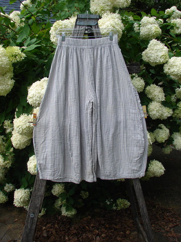 Bluefishfinder.com Barclay Gauze Crop Mojo Pant in unpainted sandy stripe, a size 0 pair of airy gauze crop pants with a gathered elastic waistband and wide, softly draped legs. The light gray striped fabric hangs from a dark wooden stand, framed by dense white hydrangea blooms and green foliage.