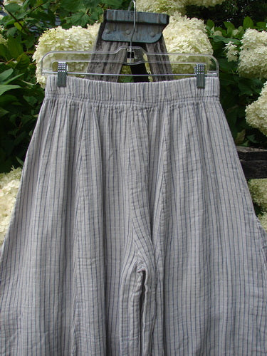 Bluefishfinder.com Barclay Gauze Crop Mojo Pant in unpainted sandy stripe, size 0, shown as lightweight gauze pants with a gathered elastic waistband and fine vertical stripes. The soft gray-beige fabric hangs in loose folds on a hanger before pale white flowers and dark wood.