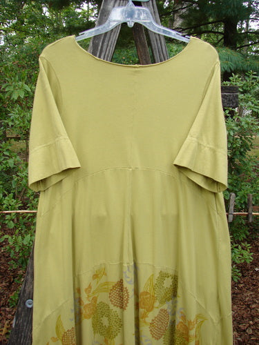 Barclay Gather Sectional Banded Petal Dress Whimsical Garden Split Pea Size 1 hanging on a wooden rack, showcasing its unique hemline, horizontal panels, and vertical gather.