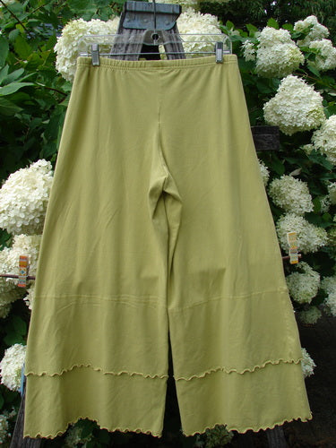Bluefishfinder.com Barclay Cotton Lycra Crop 2 Petal Pantaloon in unpainted sunshine, size 0, shown as olive-yellow cropped pants with a soft cotton-lycra drape. The wide legs fall from a simple waistband, and scalloped petal hems add a delicate layered edge against the leafy floral backdrop.