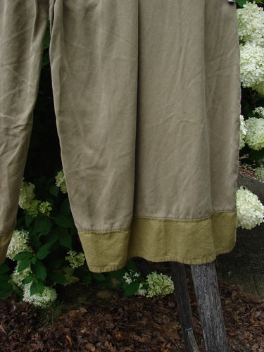 Bluefishfinder.com Barclay Lyocell Flutter Bottom Wide Leg Pant in unpainted yellow olive, size 0, with a soft drape and fluttering hem in layered olive and yellow tones. The lyocell fabric falls in wide vertical panels, framed by garden greenery and white blossoms.