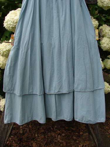 Bluefishfinder.com Barclay Batiste Fold Over Two Tier Stardust Skirt in unpainted dusky sky, size 0, with a soft blue batiste texture and layered fold-over tiers that fall in a loose, gathered silhouette. The hem sits over a darker floral backdrop, emphasizing the skirt's matte drape and gentle volume.