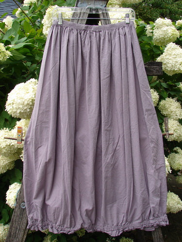 Bluefishfinder.com Barclay Batiste Airy Lawn Skirt in unpainted lavender, size 0, with a softly gathered elastic waist and a long, flowing silhouette. The lightweight batiste fabric hangs in gentle vertical folds, photographed outdoors against dense green foliage and white hydrangeas.