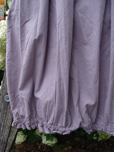 Bluefishfinder.com Barclay Batiste Airy Lawn Skirt in unpainted lavender, size 0, shown in a close-up of softly wrinkled lightweight fabric with gathered elastic hem and a loose, flowing drape. The muted purple skirt fills the frame against weathered wood and greenery.