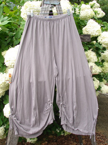 Bluefishfinder.com Barclay Crop Tie Bottom Crop 4 Square Pant in unpainted plum cloud, size 0, shown as loose gray-lavender cropped pants with a wide elastic waistband and tie hems. The lightweight fabric drapes softly, hanging against leafy white hydrangeas and weathered wood.