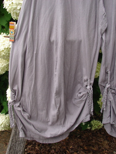 Bluefishfinder.com Barclay Crop Tie Bottom Crop 4 Square Pant in unpainted plum cloud, size 0, shown as a loose gray-lavender crop with gathered tie bottoms and long sleeves. The soft, draped fabric hangs against leafy greenery, with a small retail tag at the side.