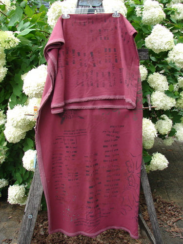 Bluefishfinder.com Barclay Heavy Weight Organic Sweatshirt Blanket Owl Forest Trimmed Burgundy OSFA drapes over a wooden A-frame, its burgundy organic fabric layered in a folded top section above a longer hanging panel. Dark owl-forest graphics and trim details add depth against the soft, matte texture, while white hydrangeas and green foliage frame the scene.