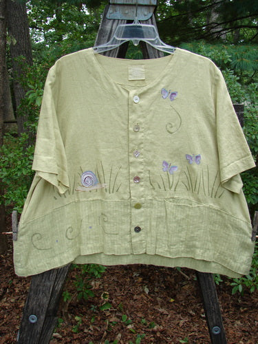 1999 Cabana Top Butterfly Grass Citron Size 2 - Green shirt featuring butterflies and flowers, shell buttons, drop pocket, and varying hemline. Light-weight textured linen with double-paneled contrasting fabric lower and Blue Fish patch.