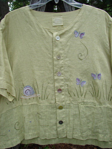 Close-up of the 1999 Cabana Top Butterfly Grass Citron Size 2, showcasing textured linen, shell buttons, a drop pocket, and a painted butterfly motif against a contrasting double-paneled lower fabric.