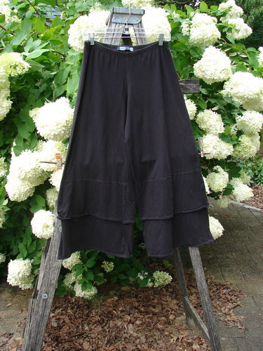 Bluefishfinder.com Barclay Cotton Lycra Crop 2 Petal Pantaloon in unpainted black, size 0, hangs from a wooden ladder amid white hydrangeas. The cropped cotton-lycra pant has a soft matte finish, a wide elastic waistband, and layered petal hems with a fluid drape.