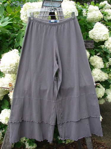 Bluefishfinder.com Barclay Cotton Lycra Crop 2 Petal Pantaloon in unpainted dusty plum, size 0, shown as wide cropped pants with a soft cotton-lycra drape, gathered elastic waist, and a layered petal hem edged in scalloped stitching. The muted plum fabric hangs from a clear hanger against white hydrangeas and green leaves, creating a natural, textured backdrop.