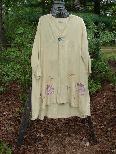 1999 Cream and Sugar Coat Pitcher Plantain OSFA displayed on a stand, featuring a V-shaped neckline, deep side pockets, oversized shell button, and unique teapot-themed design with varying lower drape.