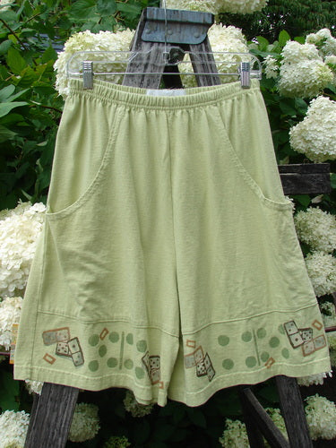Bluefishfinder.com 1998 Boxer Short Continuous Domino Clover Size 1 in pale green, with an elastic waistband, roomy front pockets, and a hem printed with domino and clover motifs. The lightweight fabric hangs from a wooden ladder amid white hydrangeas.
