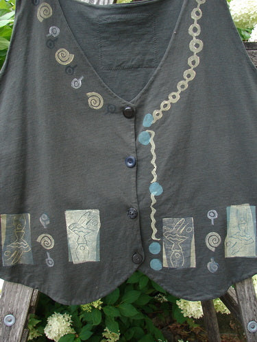 Bluefishfinder.com 1993 The Vest Dancer in black sand, size 2, is a sleeveless vest with a deep V-neck, button front, and softly curved hem. The dark fabric is decorated with spiral and block-print motifs in muted blue, cream, and gray, arranged across the chest and lower edge.