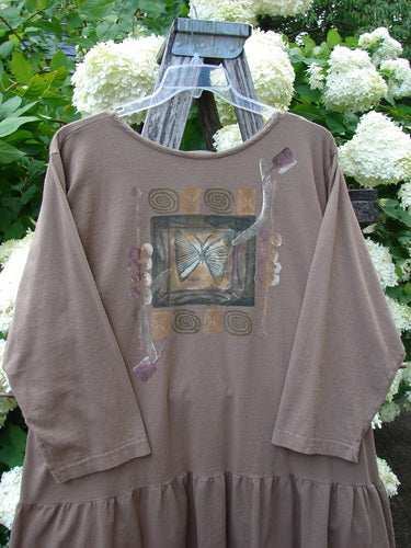 Bluefishfinder.com 1995 Clothespin Jacket Butterfly Mudpie OSFA in taupe, a loose knit garment with a wide scoop neckline, three-quarter sleeves, and a gathered hem. The front centers on a faded butterfly graphic framed by muted swirls and floral accents, draped on a rustic wooden hanger before white hydrangeas.