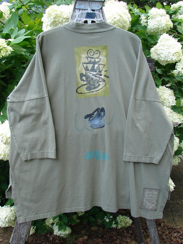 Bluefishfinder.com 1996 Message Top Tumbling Teacup Vine Size 3 in muted olive green, a long-sleeve T-shirt with a loose, oversized drape and faded graphic prints down the front. The soft cotton fabric hangs from a hanger, with a small chest print, larger central teacup motif, and a square hem label