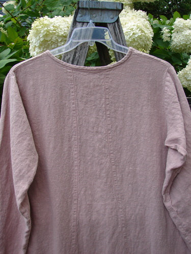 Bluefishfinder.com 1998 Botanicals Thostle Dress Single Tulip Mallow Size 1 in dusty mauve, a long-sleeve dress with a round neckline and soft, wrinkled fabric. It hangs on a clear hanger before pale hydrangeas and dark wood, creating a muted garden backdrop.