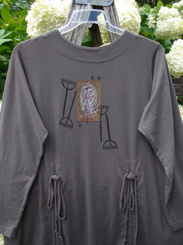 Bluefishfinder.com 1998 Cornucopia Dress Fall Garden Eggplant Size 1 in muted eggplant gray, a long-sleeve dress with a soft drape, crew neckline, and gathered side ties. The front shows a centered cornucopia-style graphic in earthy tones, hanging outdoors on a clear hanger among green leaves and white flowers.