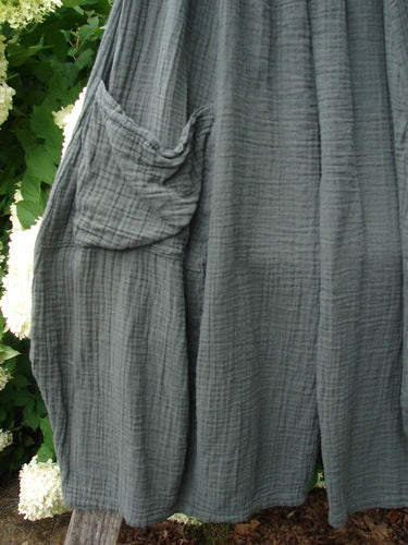 Bluefishfinder.com Barclay Gauze Crop Mojo Pant in unpainted evergreen, size 1, shown in a softly crinkled gauze fabric with a loose cropped silhouette and a gathered side pocket. The muted gray-green texture falls in layered folds against leafy greenery.