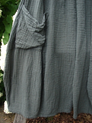 Bluefishfinder.com Barclay Gauze Crop Mojo Pant in unpainted evergreen, size 1, shown in textured gauze with a softly crinkled drape and a loose cargo pocket on the side. The cropped hem falls in layered folds, and the muted green-gray fabric fills the frame against a natural outdoor backdrop.