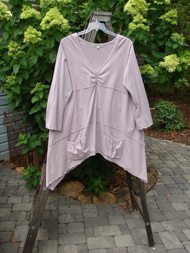 Barclay Cotton Lycra Vertical Gather Drop Pocket Dress Unpainted Lavender Size 2 hanging on a rack, showcasing a deeper V-shaped neckline, oversized front gathered pockets, and sectional horizontal panels.