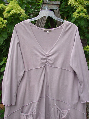 Barclay Cotton Lycra Vertical Gather Drop Pocket Dress on a swinger, showcasing its deep V-neckline, oversized front pockets, and sectional horizontal panels, in a widening shape with a varying hemline.