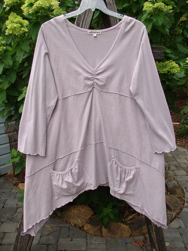 Barclay Cotton Lycra Vertical Gather Drop Pocket Dress Unpainted Lavender Size 2 hanging on a clothesline, showcasing its long sleeves, deeper V-shaped neckline, and oversized front gathered pockets.