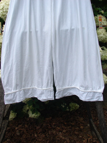 Barclay Flutter Bottom Pocketless Pant in unpainted white, size 1, shown as loose white pants with wide flutter hems, a soft draped texture, and a pocketless front. The legs hang symmetrically in the frame against dark foliage, emphasizing the airy fabric and clean, minimal silhouette.