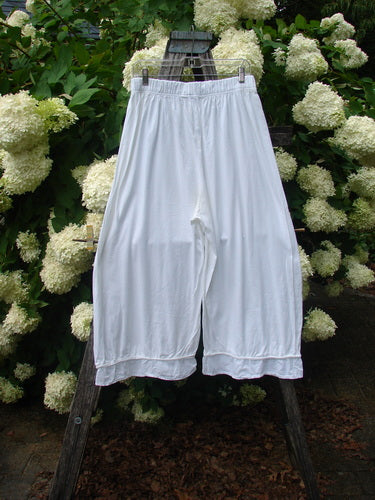 Barclay Flutter Bottom Pocketless Pant in unpainted white, size 1, hangs from a wooden ladder against dense white hydrangea blooms and dark green foliage. The lightweight fabric falls in a loose, wide leg with a fluttered hem and an elastic waistband.