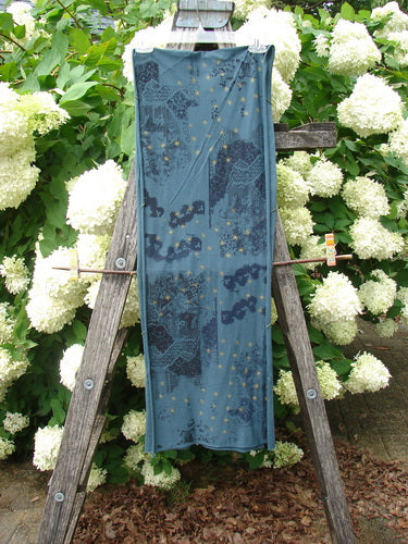 Bluefishfinder.com Barclay Diagional Scarf Wrap Stary Night Garden Blue Hunter OSFA, a long blue wrap with a diagonal drape and scattered starry floral pattern. It hangs vertically from a weathered wooden ladder amid dense white blossoms and green foliage, creating a layered outdoor display.