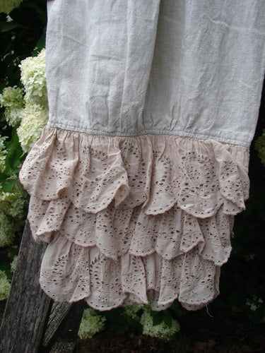 Magnolia Pearl Homespun Linen Ruffle Eyelet Bloomer in natural OSFA, shown in pale linen with layered eyelet ruffles at the hem. The soft, textured fabric hangs against dark wood and leafy white blossoms, creating a muted, rustic contrast.