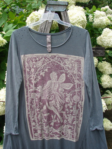 Bluefishfinder.com Magnolia Pearl Cotton Jersey Dylan Dress Fairy Ozzy OSFA in faded charcoal cotton jersey, with a relaxed long-sleeve silhouette and a large faded mauve floral graphic framed on the front. The dress hangs from a clear hanger before white hydrangeas and weathered wood, creating a soft, rustic backdrop.