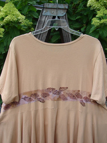 1997 Ocean Pearl Dress Leaf Band Driftwood Size 2: A tan organic cotton dress with brown leaf patterns, featuring a rounded neckline, slight empire waist, and a tiny painted pocket, displayed on a hanger.