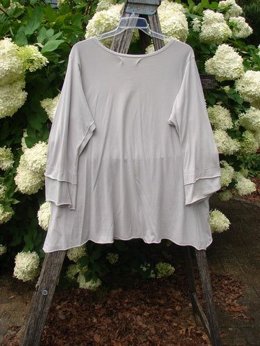 Bluefishfinder.com Barclay Petal Sleeve A Line Tunic Falling Fern Birch Bark Size 1 in soft birch bark beige, a loose A-line top with petal sleeves and a gently curved hem. The lightweight fabric hangs from a clear hanger against white hydrangeas and dark greenery.