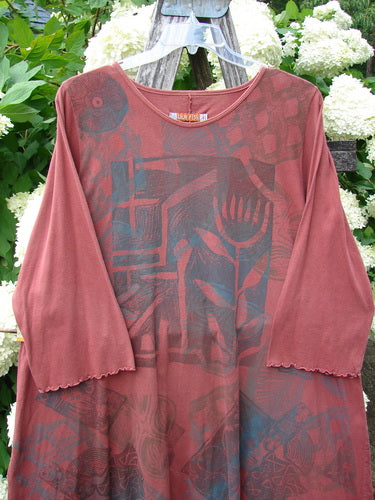 Bluefishfinder.com Barclay Three Quarter Sleeve Color Wheel Tunic Tulip Dream Clay Size 1 in muted clay rose, with three-quarter sleeves, a rounded neckline, and an allover tonal graphic print. The soft, drapey tunic hangs on a hanger, its sheer layered fabric set against bright white flowers and green foliage.