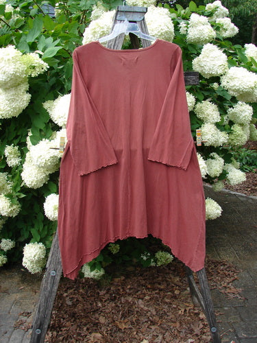 Bluefishfinder.com Barclay Three Quarter Sleeve Color Wheel Tunic Tulip Dream Clay, a clay-colored tunic with three-quarter sleeves, raw-edged hems, and a loose draped silhouette, displayed on a hanger against white hydrangeas.