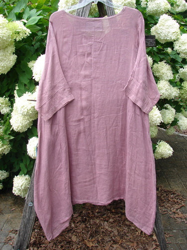 Bluefishfinder.com Barclay Linen Wave Pocket Dress Dried Sprig Tulsi Rose Size 1, a dusty rose linen dress with a relaxed, oversized drape and softly wrinkled texture. It hangs front-facing from a wooden stand, showing wide short sleeves, a round neckline, and an uneven hem.