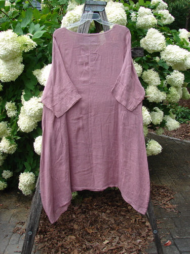 Bluefishfinder.com Barclay Linen Wave Pocket Dress Dried Sprig Tulsi Rose Size 1, a dusty rose linen dress with a softly crinkled texture, wide boat neckline, and flowing wave-shaped pockets. It hangs centered on a wooden frame against white hydrangeas and green foliage.