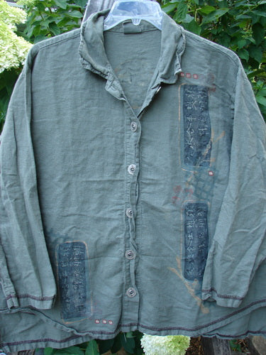 Barclay Hemp Cotton Metal Button Workshirt Asian Script Army Size 0 displayed on a hanger, features exterior contrasting stitchery, full metal button front, shirttail hemline, and stand-up collar.