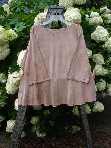Bluefishfinder.com Barclay Three Quarter Sleeved Cafe Tee Giant Sunflower Mottled Pumpkin Size 1 in mottled pumpkin, a loose three-quarter-sleeve top with raw, scalloped hems and a soft, draped texture, hanging from a rustic wooden easel amid white hydrangeas and dense green foliage.