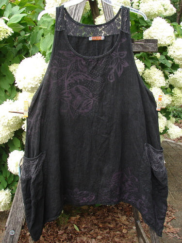 Bluefishfinder.com Barclay Summercloth Lace Two Pocket Pinafore in Moody Night Bloom Black, a loose black sleeveless dress with a sheer lace yoke and two oversized side pockets. The dark floral pattern is softly visible across the fabric, hanging in front of leafy white hydrangeas.